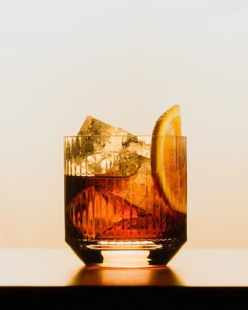 A negroni cocktail in a glass with ice and an orange slice, set against a neutral background, showcases a classic drink presentation.
