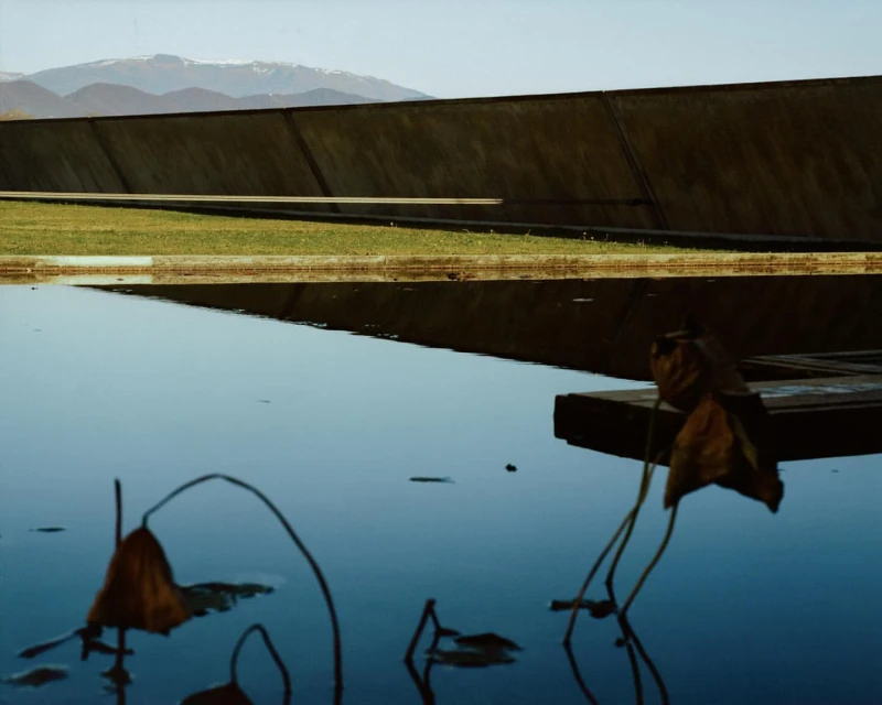 Scenic view of water reflecting a concrete structure, complemented by dry leaves, creating a serene and contrasting landscape.
