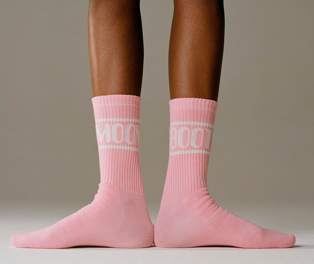 Close-up of lower legs wearing ribbed pink socks with white typography standing against a neutral studio background.