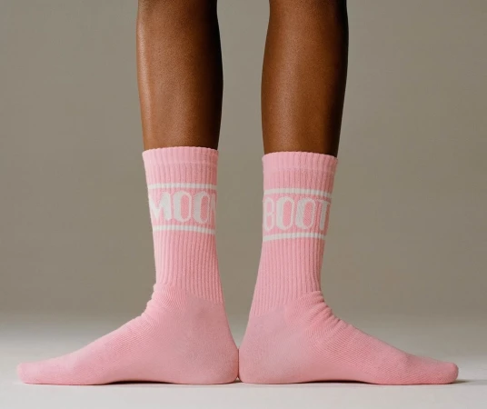 Close-up of lower legs wearing ribbed pink socks with white typography standing against a neutral studio background.