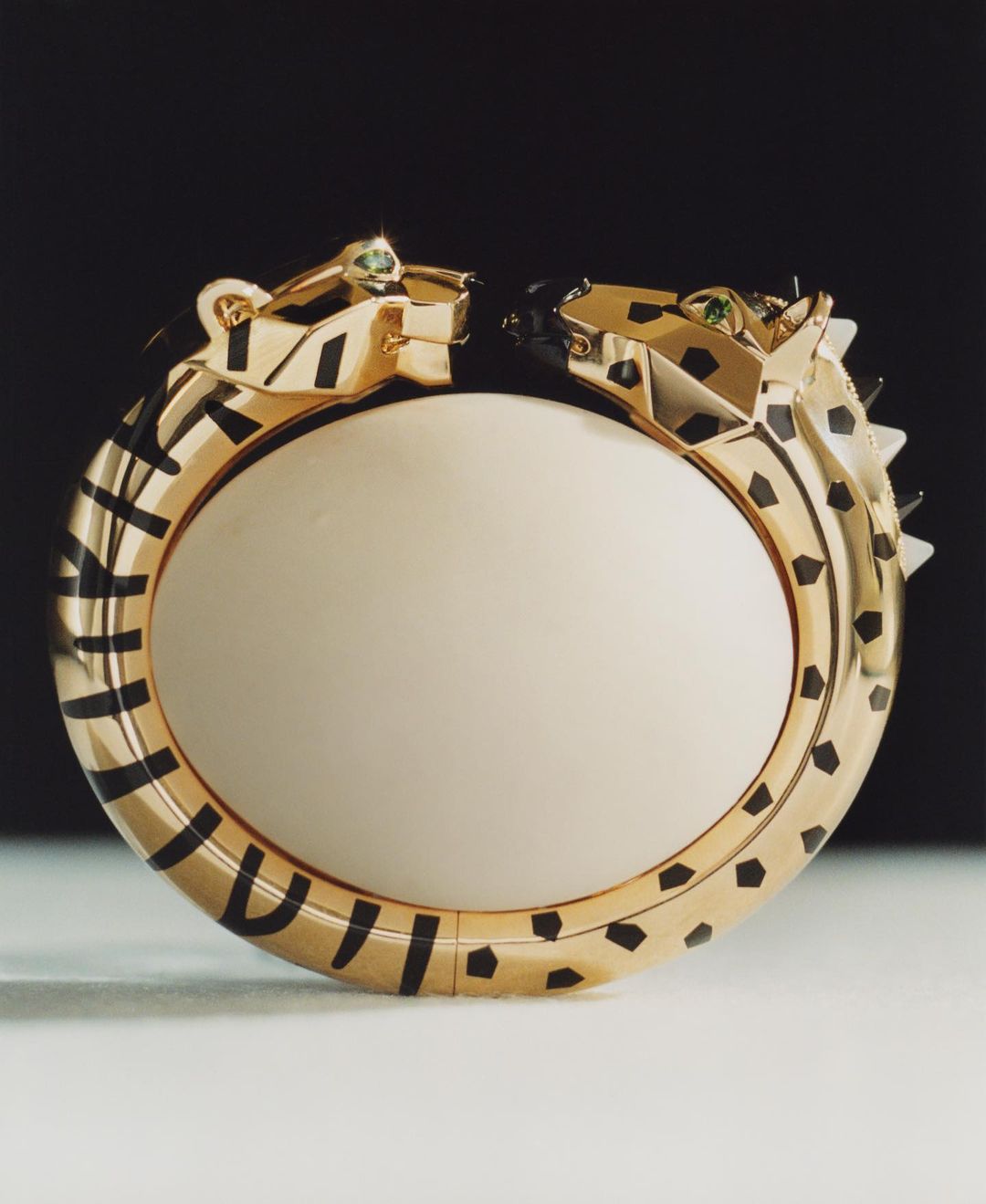 Gold bangle bracelet featuring two panther heads, set against a gradient gray to black background, showcasing luxury jewelry design.