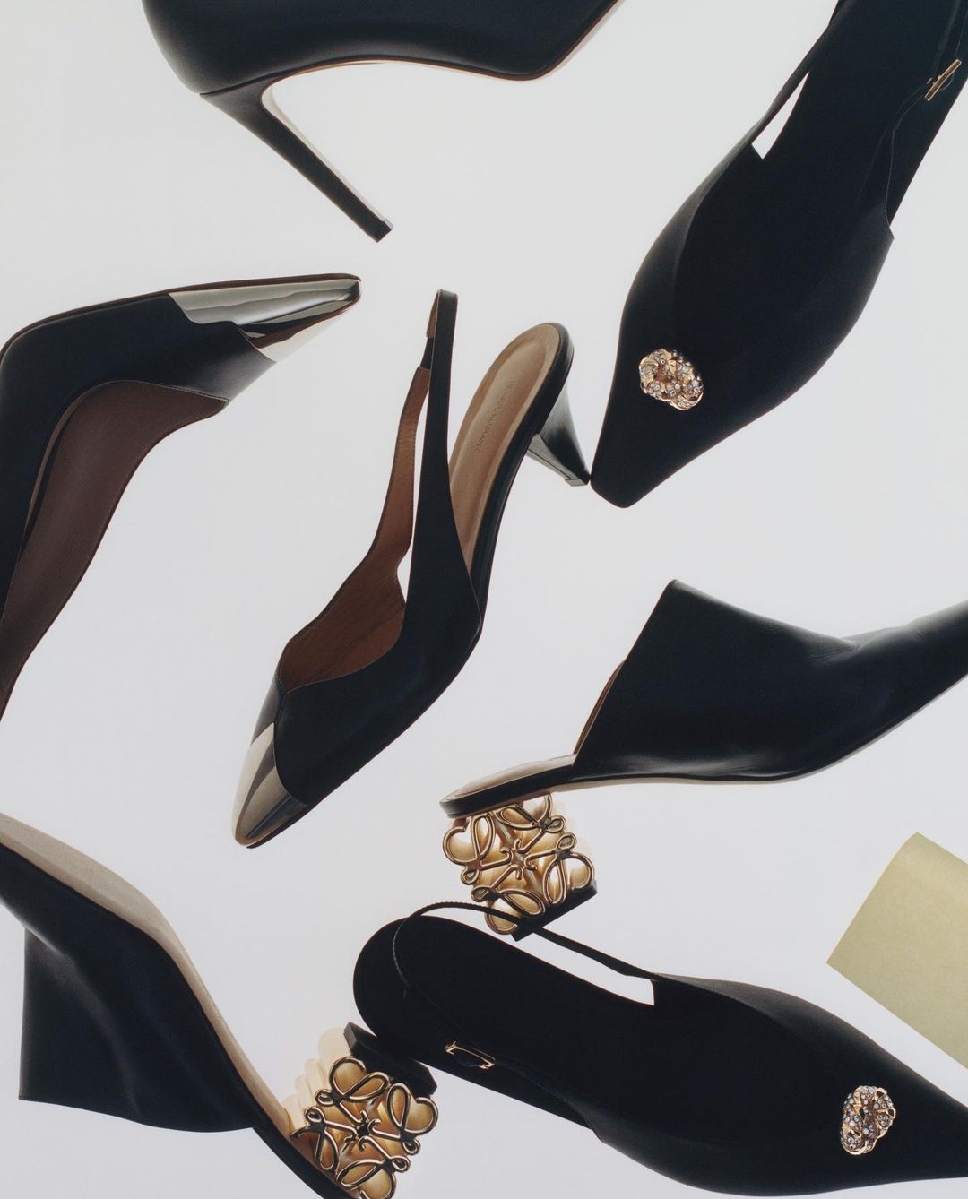 Arrangement of assorted black high heel shoes with gold decorative elements against a white background in a studio fashion shot.