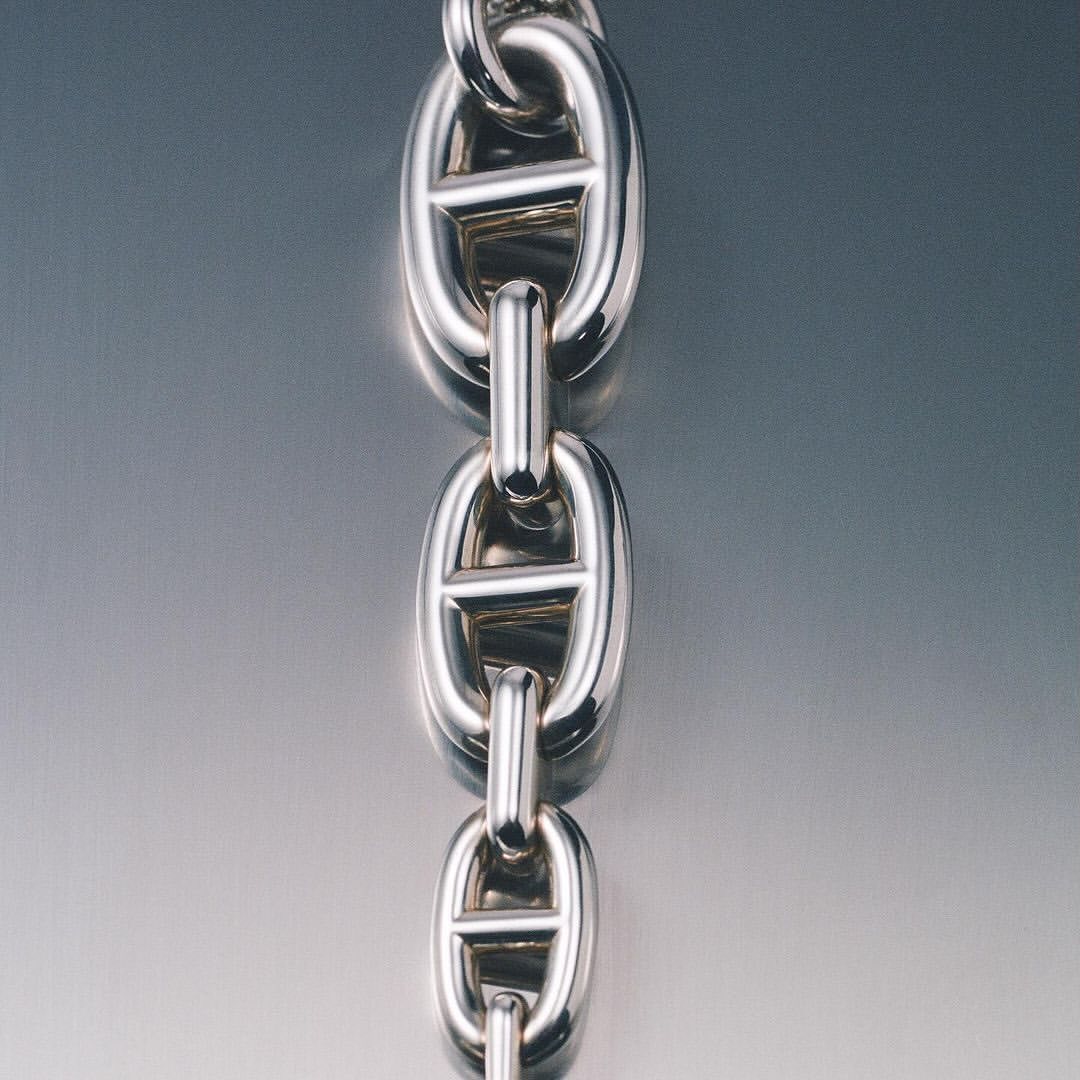 Close-up of a silver chain necklace, showcasing interlocking links with a reflective background and a smooth, polished finish.