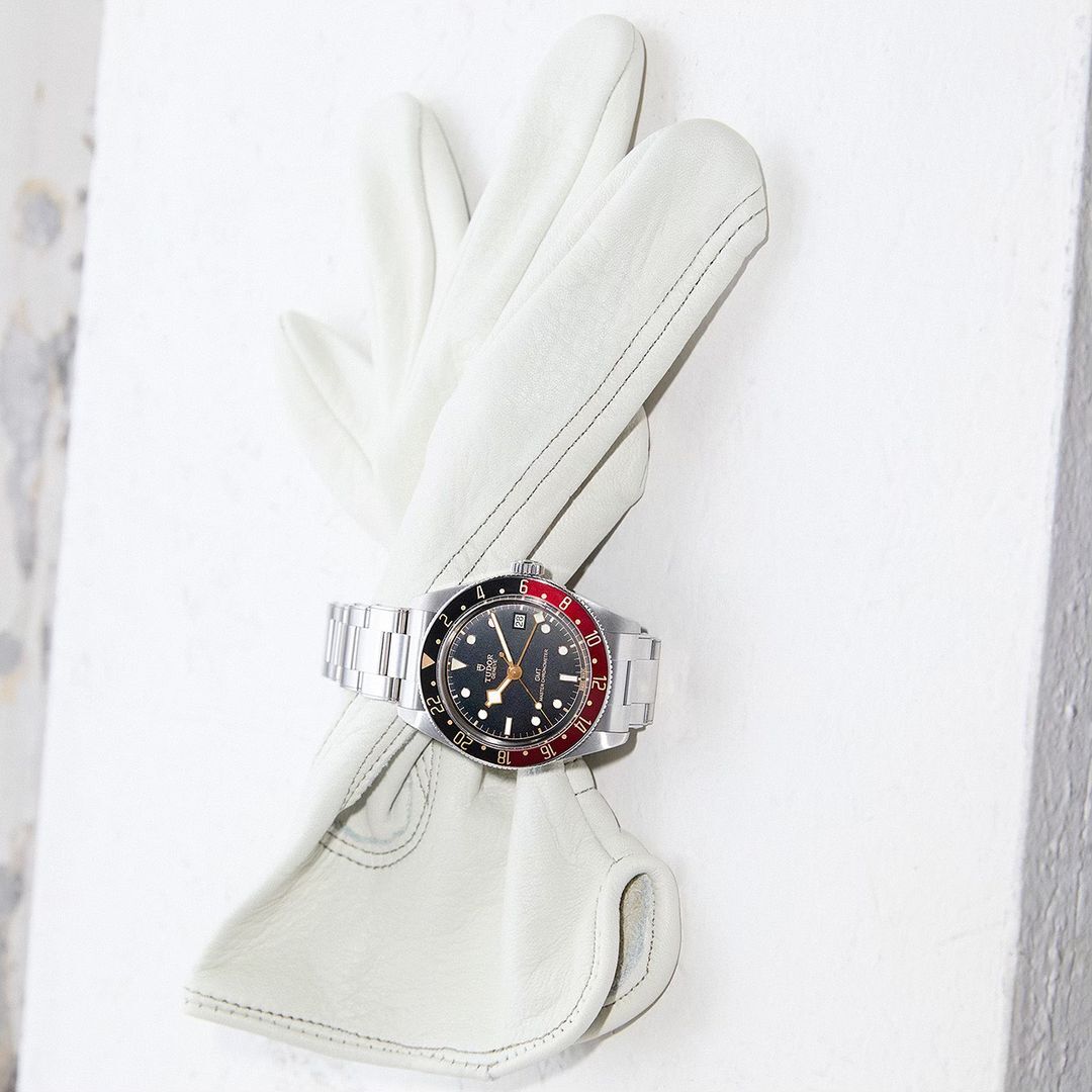 Wristwatch with a stainless steel bracelet displayed on a folded white leather glove against a textured white surface. Timepiece details.