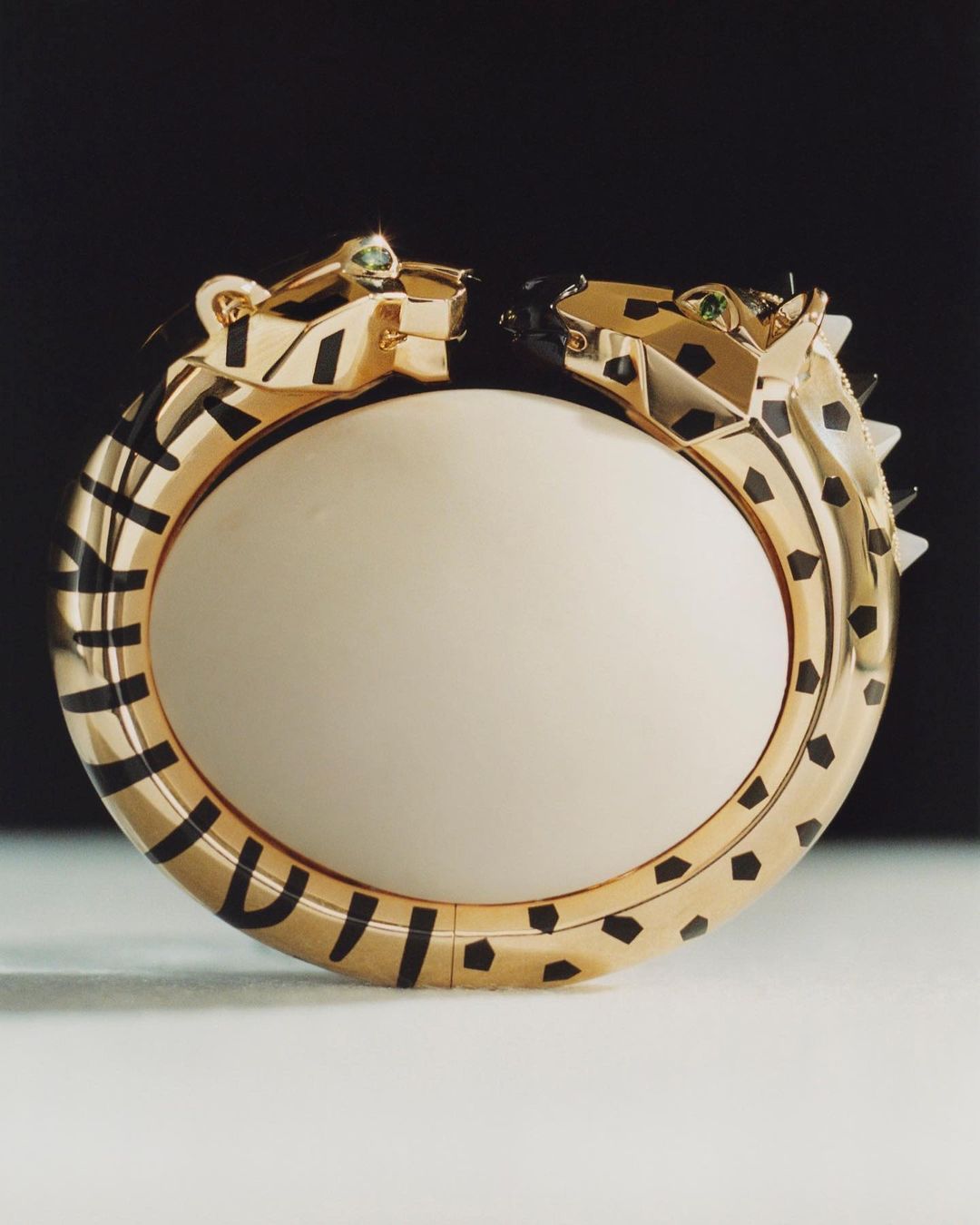 Close-up of a gold bangle bracelet featuring a jaguar head at each end, adorned with black enamel stripes and green gemstone eyes.