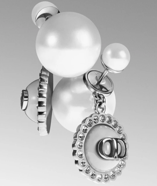 Close-up of Dior Tribales earrings featuring white pearls and a silver-tone finish with crystal accents on a gradient grey background.