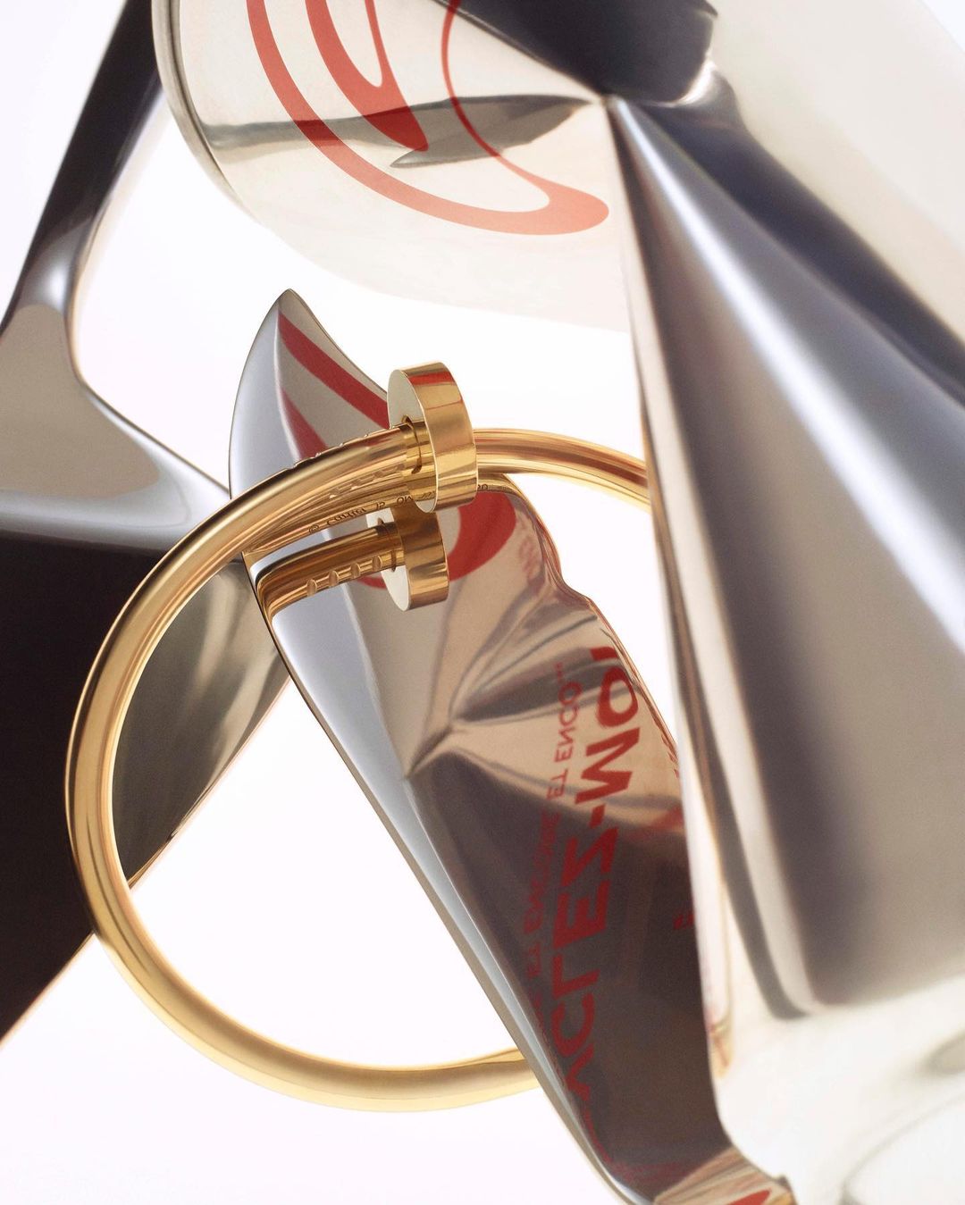 Abstract close-up of a gold ring intersecting distorted silver tubes with red markings against a bright white background, studio photography.