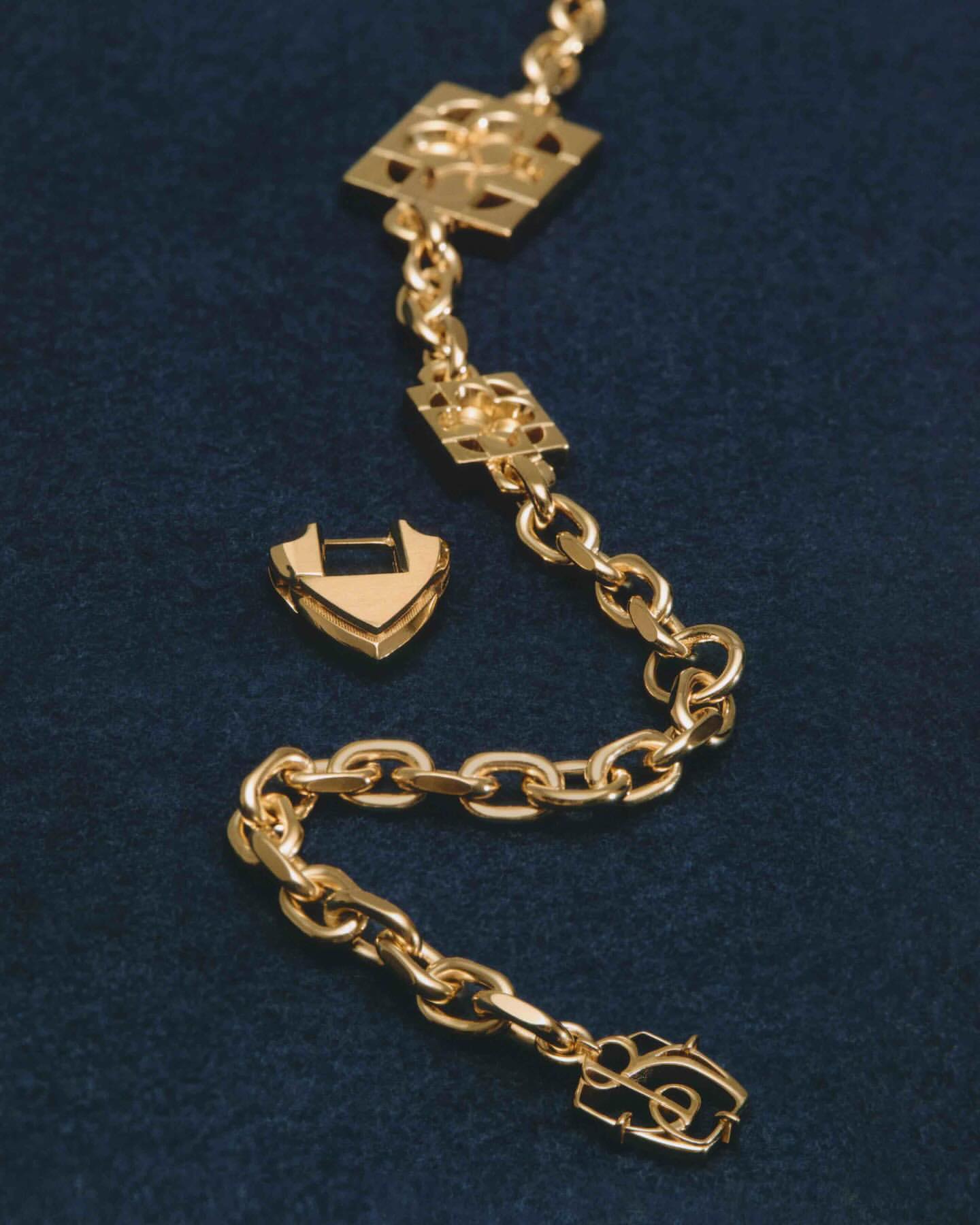 Golden chain link necklace with decorative geometric charms on a blue velvet surface, showcased in a close-up studio product shot.