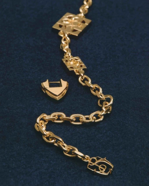 Golden chain link necklace with decorative geometric charms on a blue velvet surface, showcased in a close-up studio product shot.