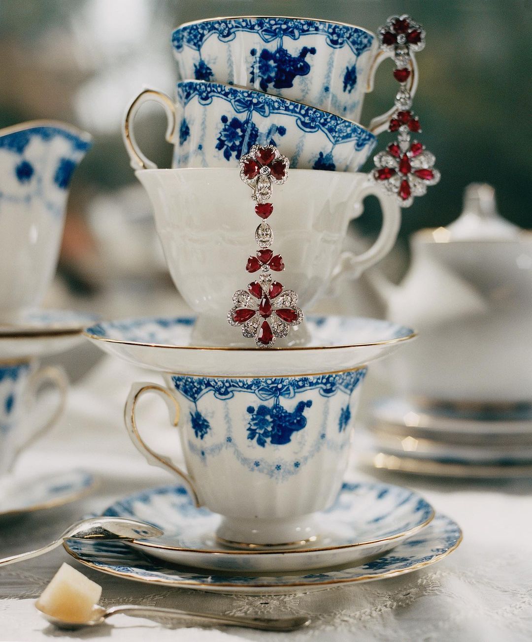 Close-up of stacked teacups with blue floral designs and ruby and diamond drop earrings, creating an elegant and decorative still life.