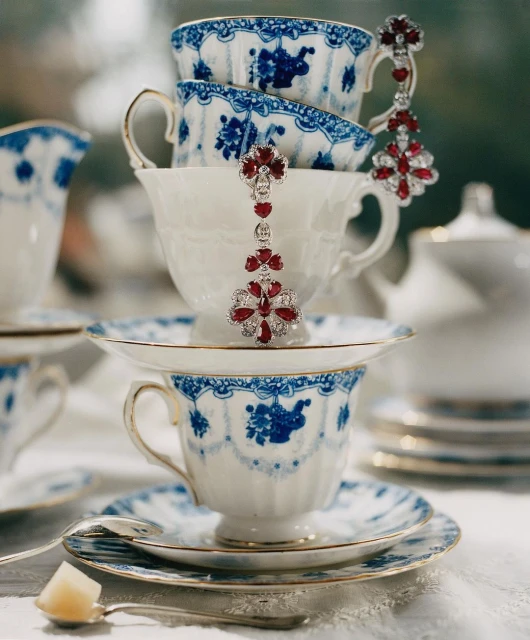 Close-up of stacked teacups with blue floral designs and ruby and diamond drop earrings, creating an elegant and decorative still life.