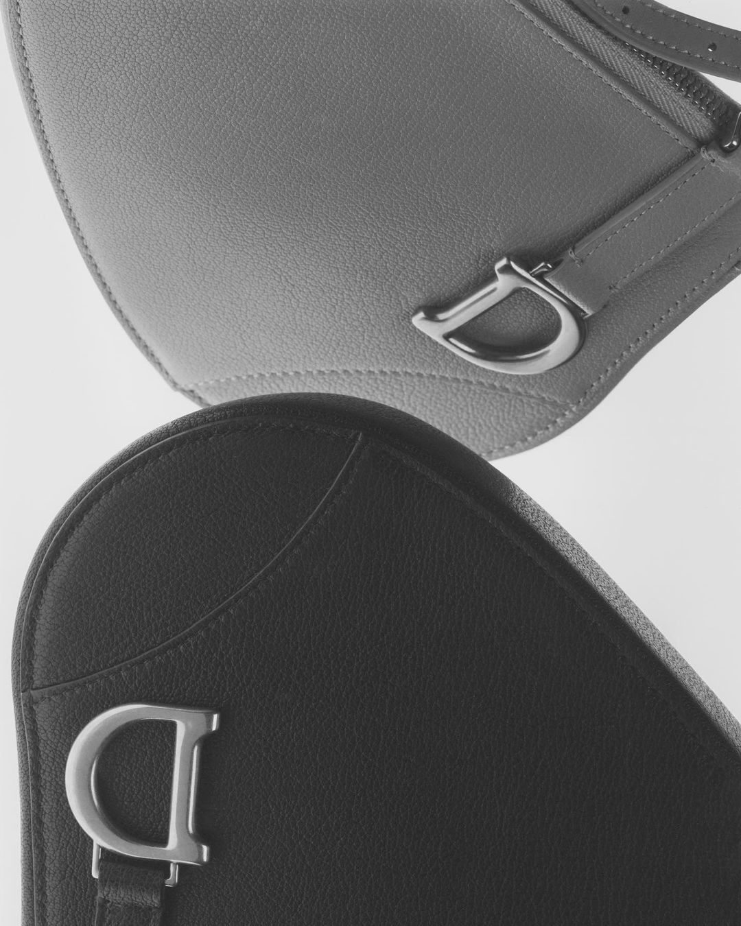Two black and gray saddle bags are displayed in a product shot with silver D-shaped accents, conveying luxury fashion.