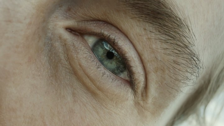 Close-up shot of a person's eye with blue and green hues, capturing detailed textures of the surrounding skin and brow.