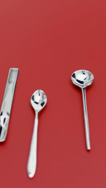 Three silver metal spoons of various sizes lie on a flat red surface, offering a clean and minimalist aesthetic.