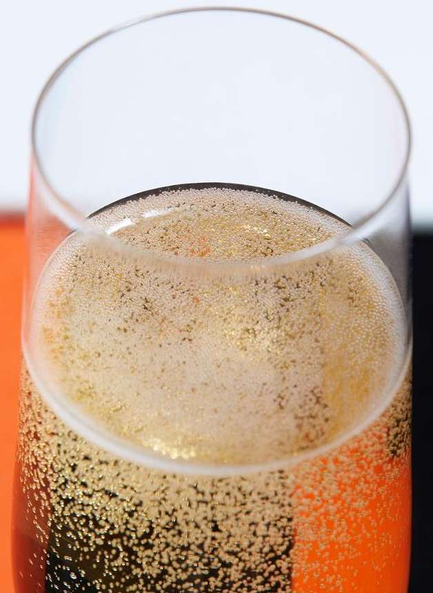 Close-up of a clear champagne flute filled with sparkling champagne, showcasing gold liquid and tiny bubbles, atop a colorful surface.