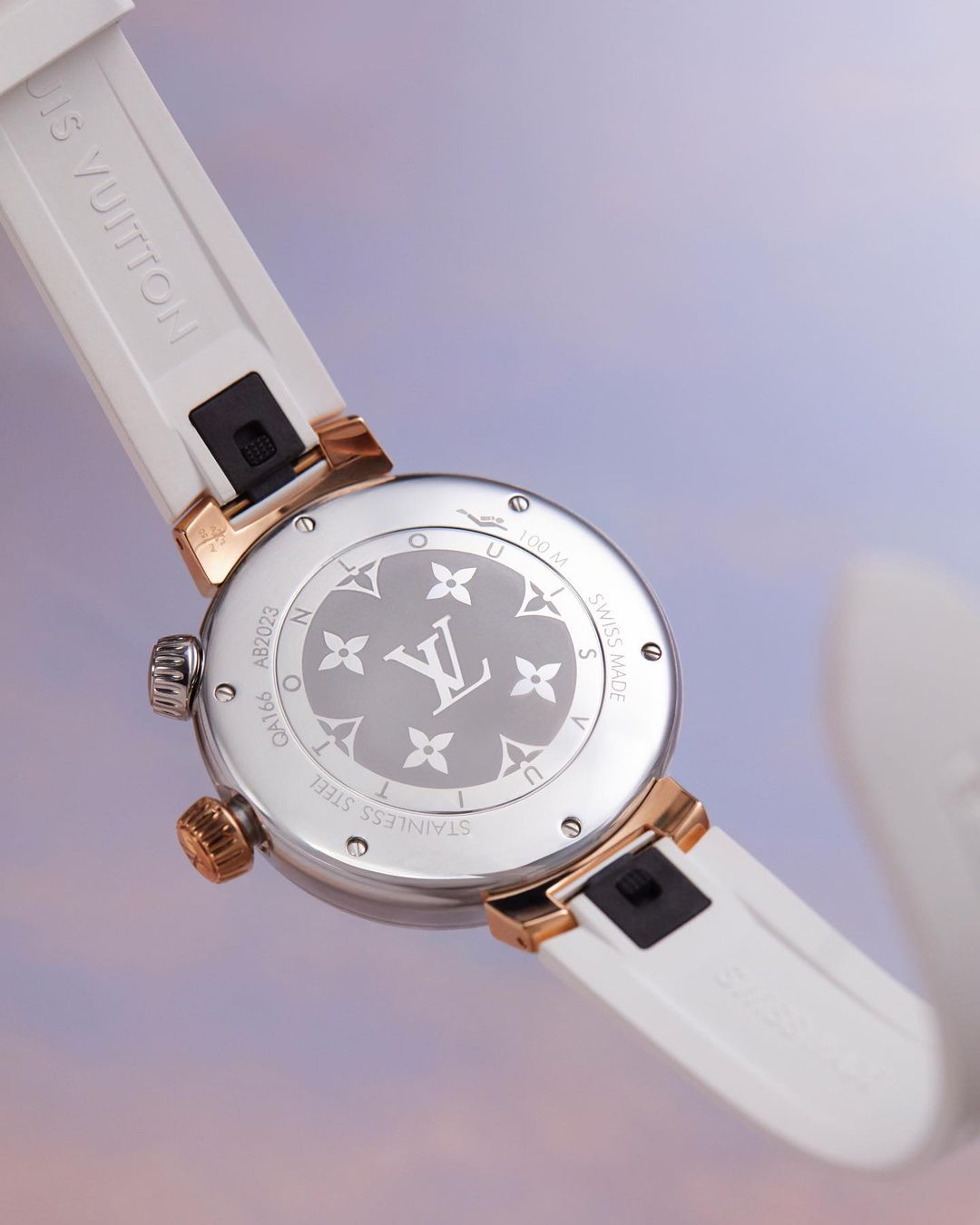 Close-up of a Louis Vuitton watch featuring a white band and a silver and gold face with the LV logo, set against a soft, colorful backdrop.