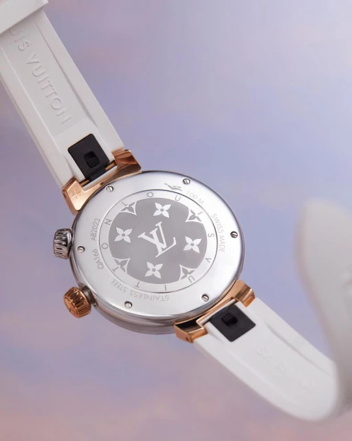 Close-up of a Louis Vuitton watch featuring a white band and a silver and gold face with the LV logo, set against a soft, colorful backdrop.