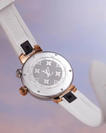 Close-up of a Louis Vuitton watch featuring a white band and a silver and gold face with the LV logo, set against a soft, colorful backdrop.
