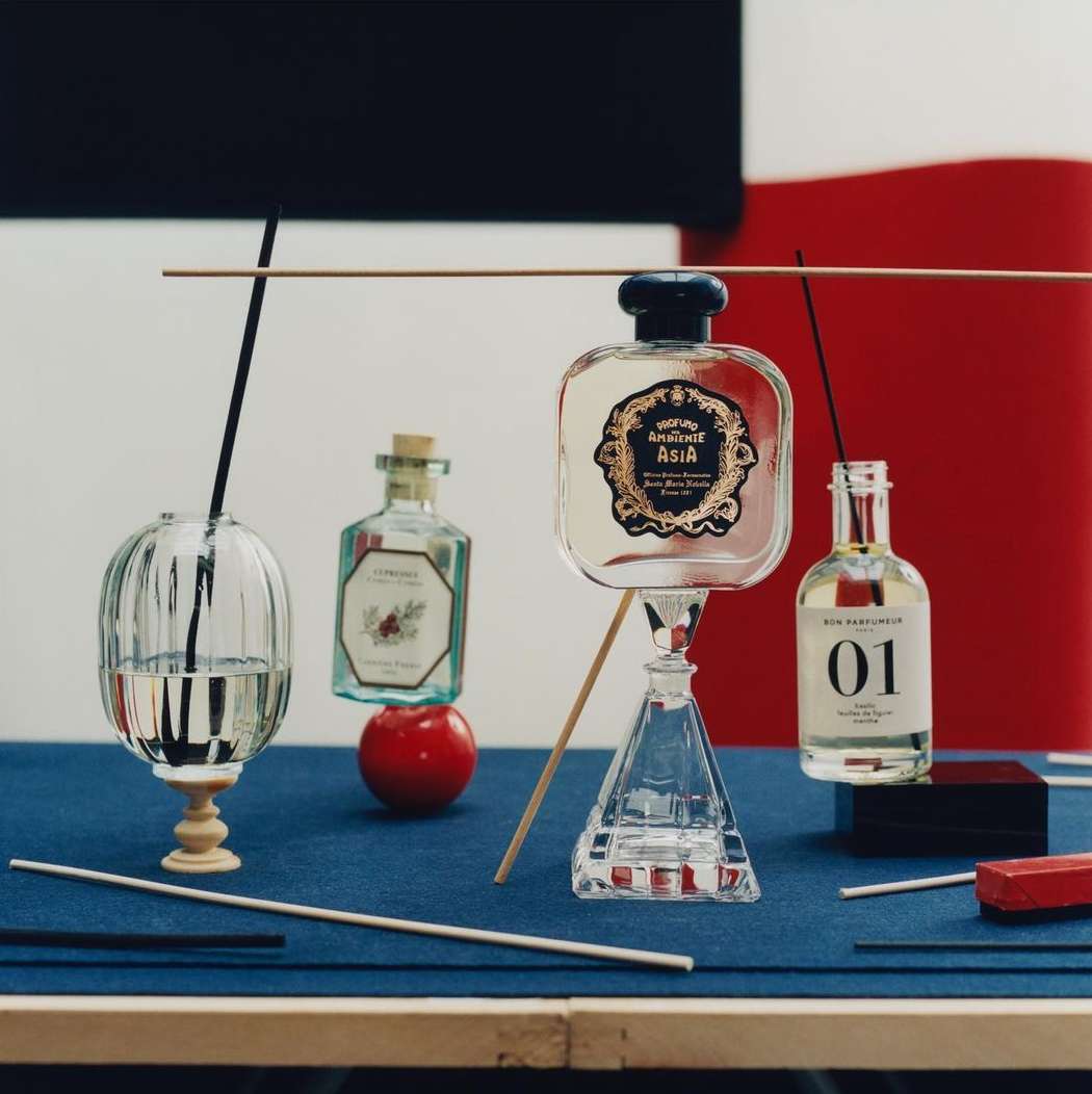 Still life of perfume bottles on blue surface, featuring various shapes and designs against a backdrop of red, white, and black.