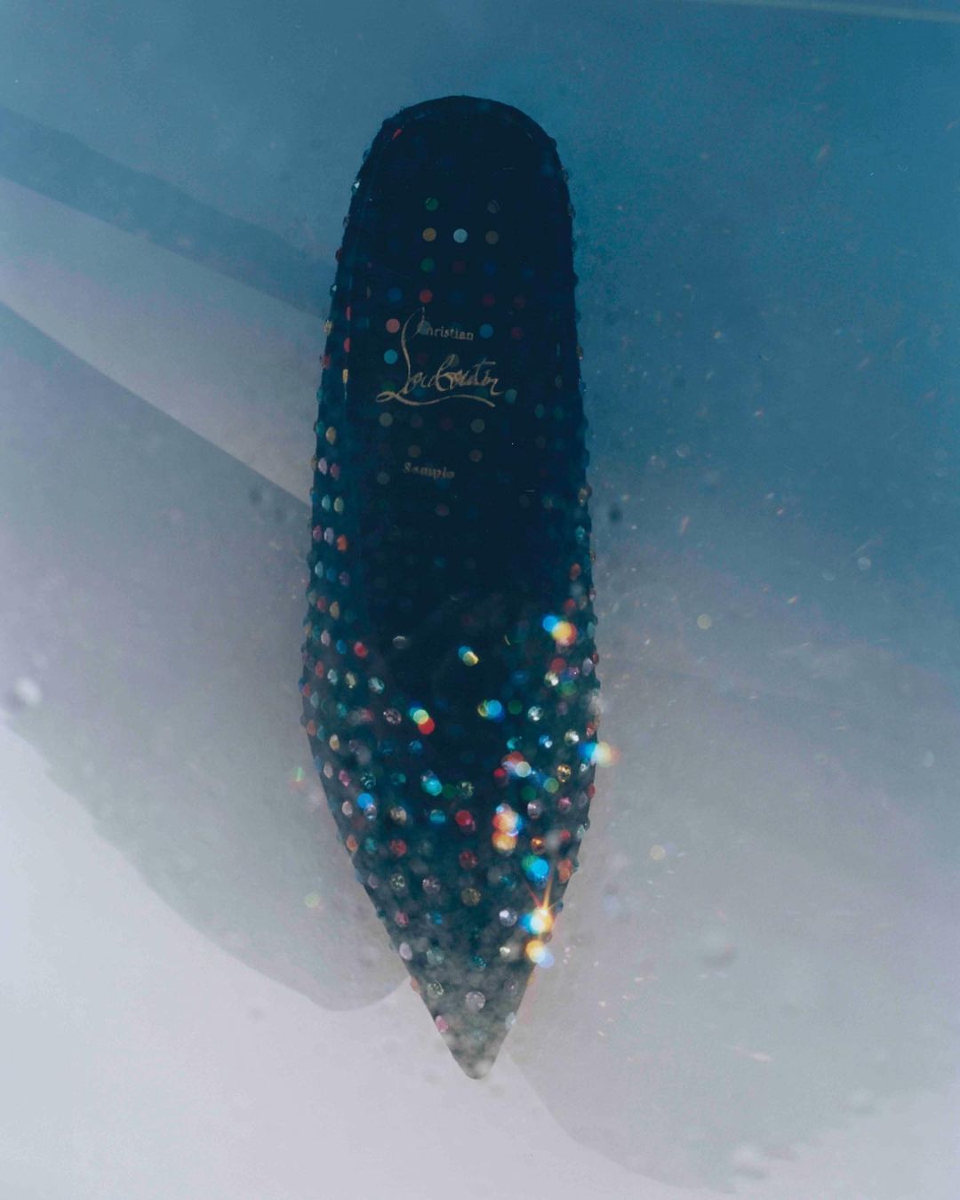 Elegant black Christian Louboutin stiletto heel with colorful bead embellishments against a light blue and white background.