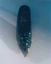 Close-up of a dark crystal-embellished high heel shoe submerged in water with light refractions by Matzo matzo