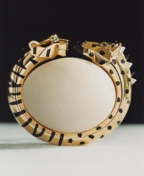 Close-up product photography of a gold panther bangle bracelet with black enamel spots against a dark background