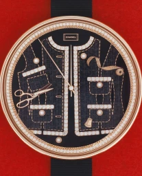 Close-up of a luxury wristwatch dial featuring miniature gold jacket, diamond trim, scissors, and sewing tools against a red backdrop