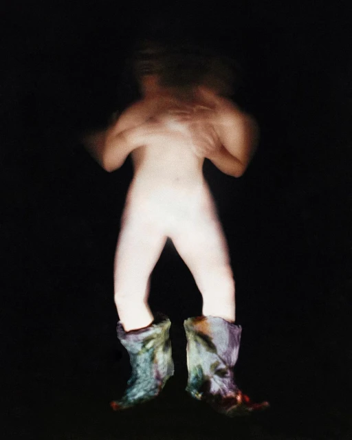 Abstract studio shot of a nude figure wearing a pair of multi-colored boots against a dark background with motion blur.