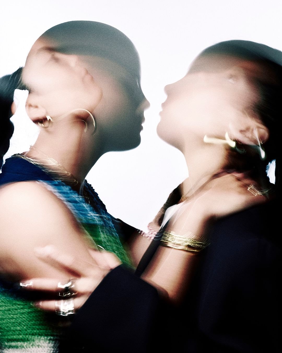 Close-up of two women with blurred motion, face to face with gold jewelry. The blurred motion gives a sense of movement and energy.