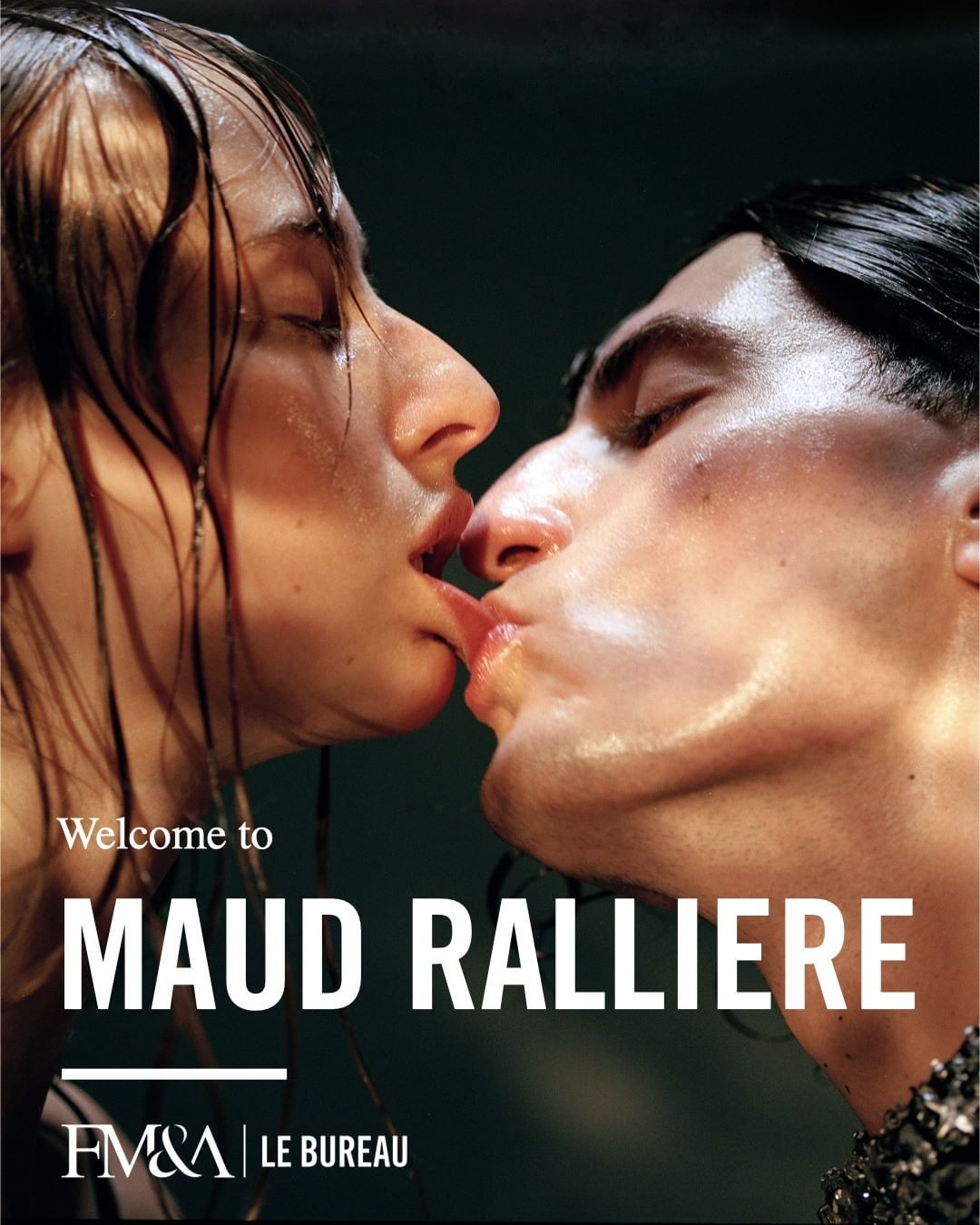 Close-up portrait of two people, an adult male and female, kissing with visible skin texture and studio lighting against a dark background.