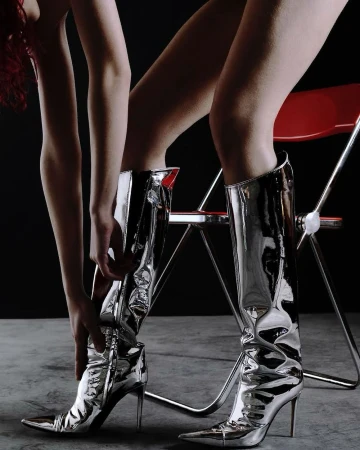 Woman's legs in shiny silver knee-high stiletto heel boots with a black background and a red metal chair create a fashion-forward studio shot.