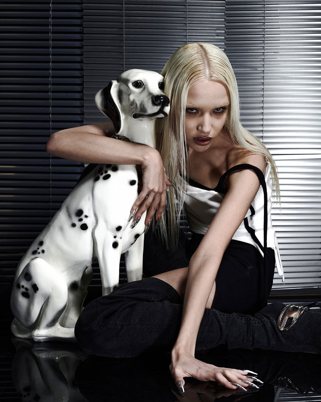 Young woman with long blonde hair poses indoors with a Dalmatian statue, showcasing fashion, beauty, and studio photography.