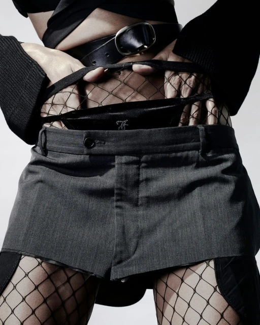 Torso shot of a fashion model in stylish grey shorts, a black top and fishnet stockings posing in a studio setting with a white background.