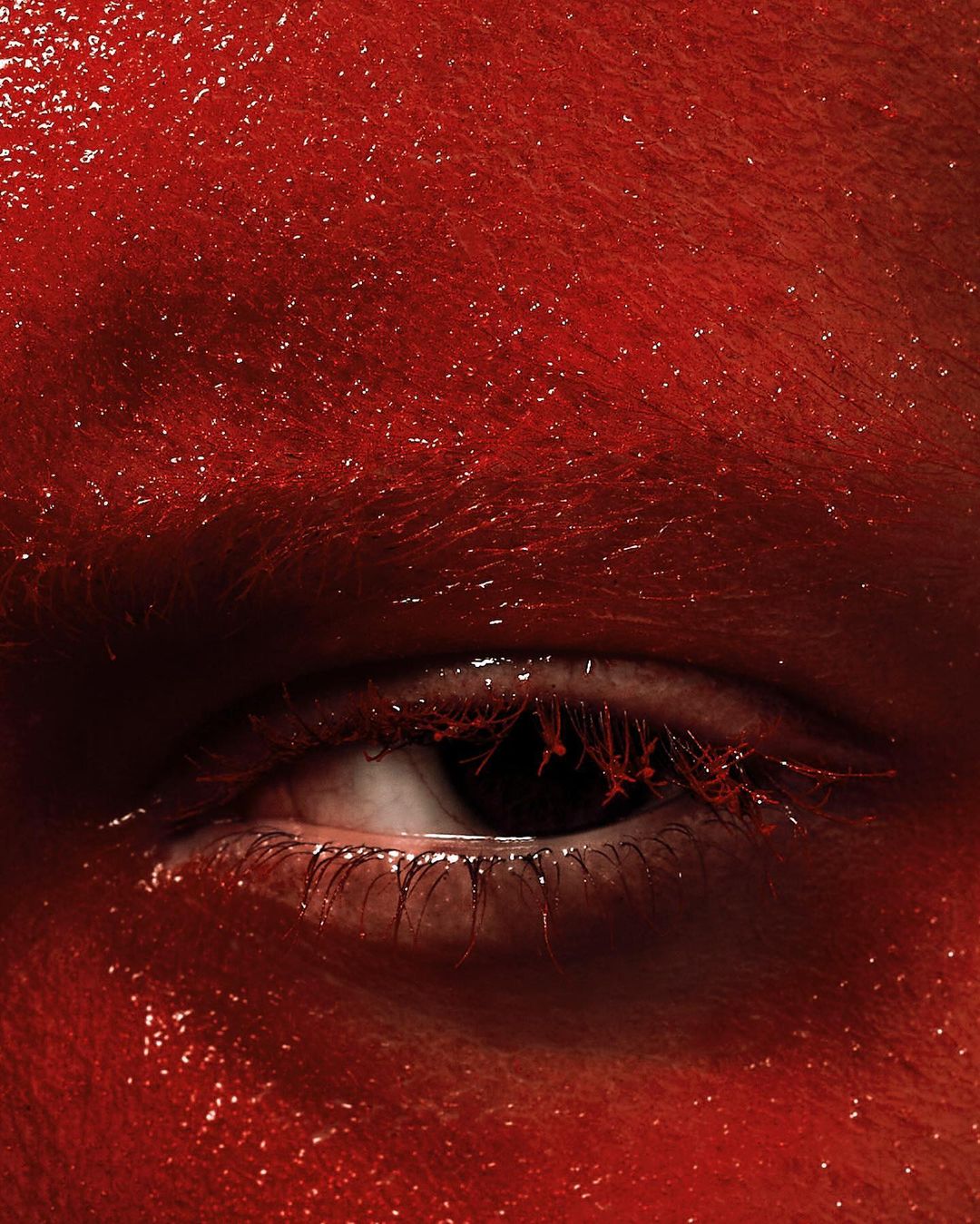 Macro shot of an eye and face covered in shiny red paint, creating a striking and textured visual.