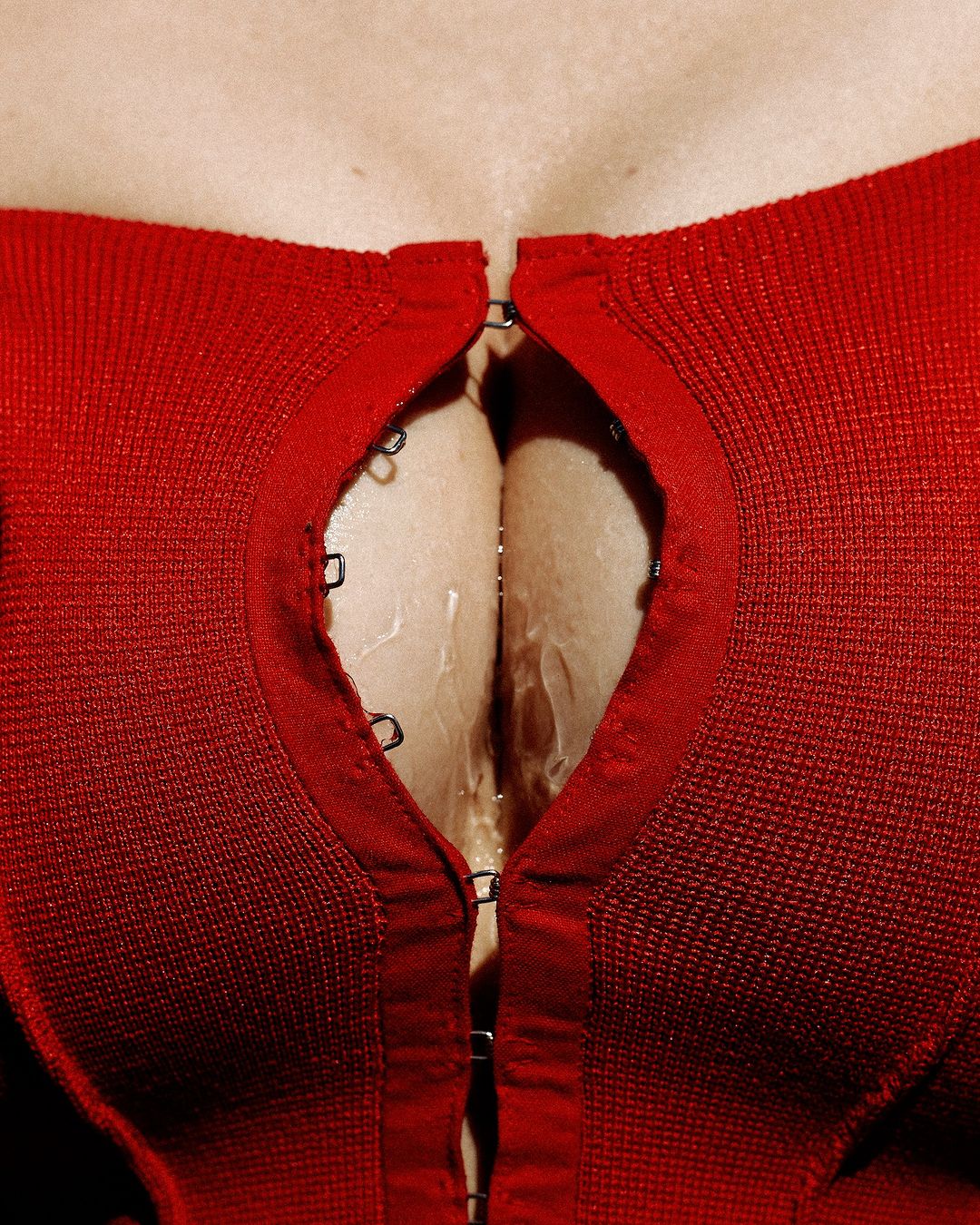 Close-up of a light-skinned woman's upper chest and red knitted top, partially open with metal hook-and-eye closures.