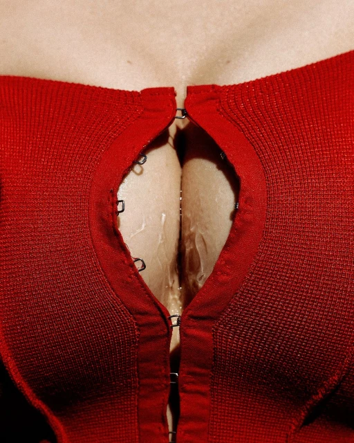 Close-up of a light-skinned woman's upper chest and red knitted top, partially open with metal hook-and-eye closures.