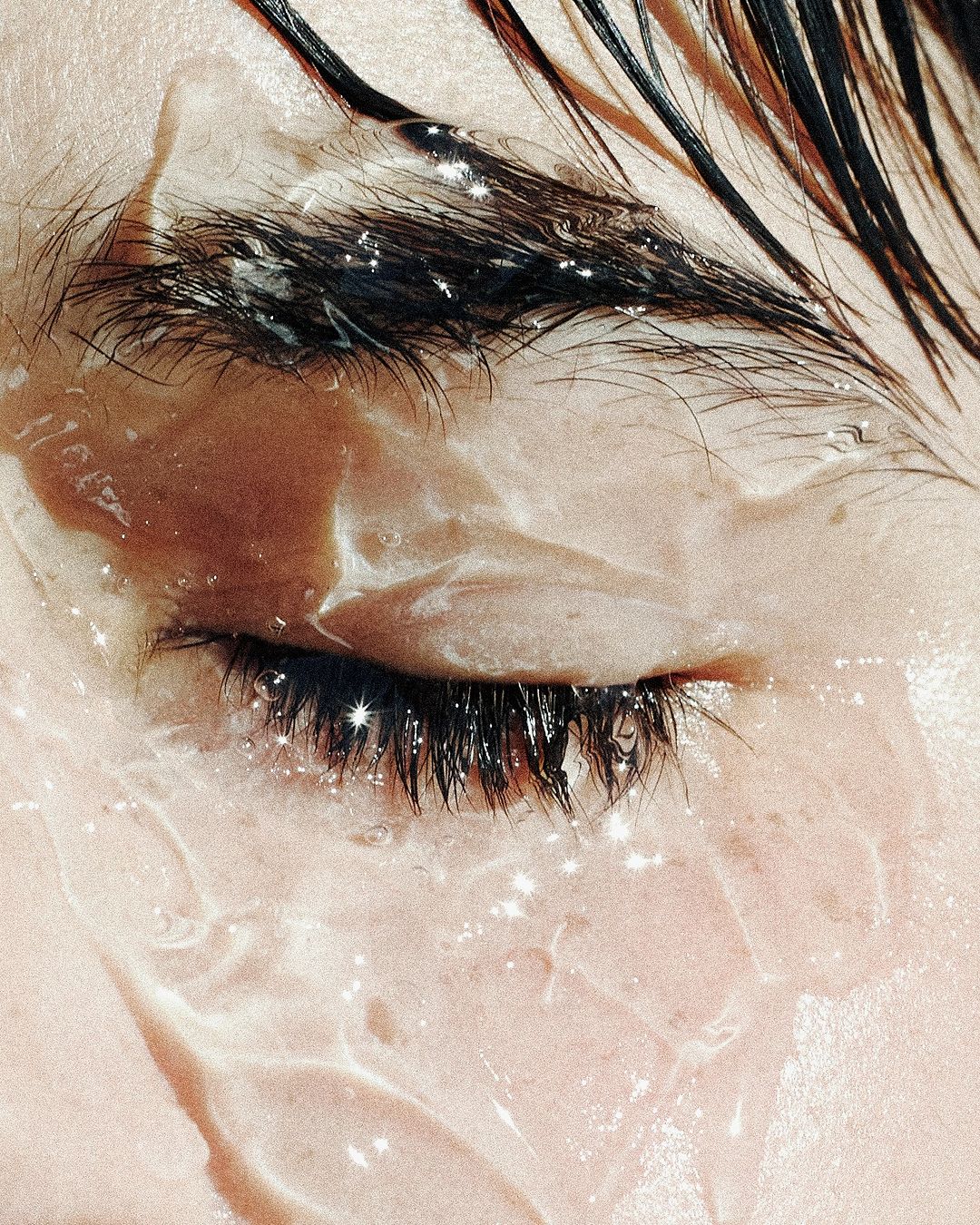 Close-up shot of a person's eye, eyebrow, and forehead with wet skin. Focus on natural beauty and skincare in a bright, textured setting.