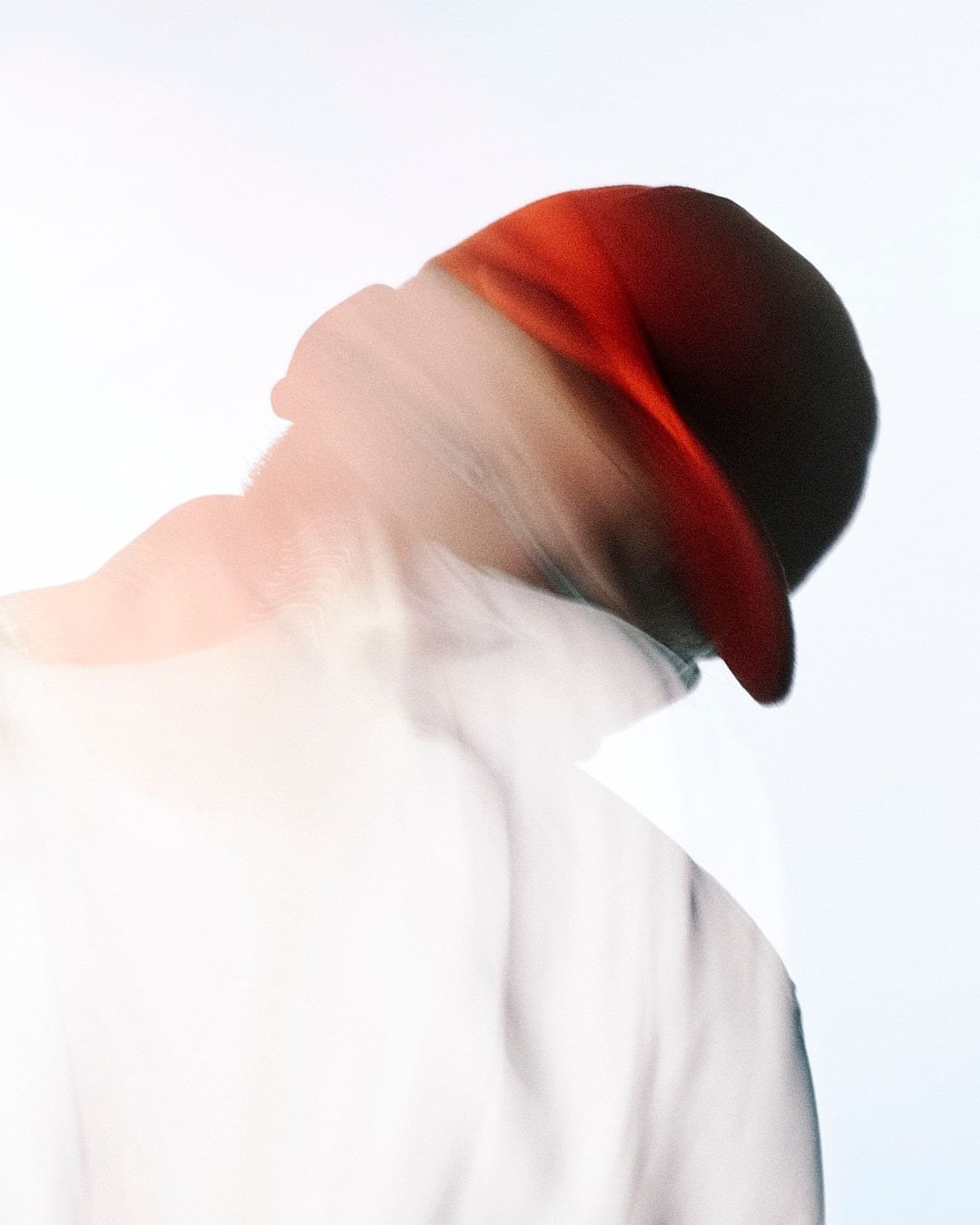 Abstract portrait of an adult male wearing a baseball cap. The photo uses blurring and a bright, high-key light to create a modern effect.