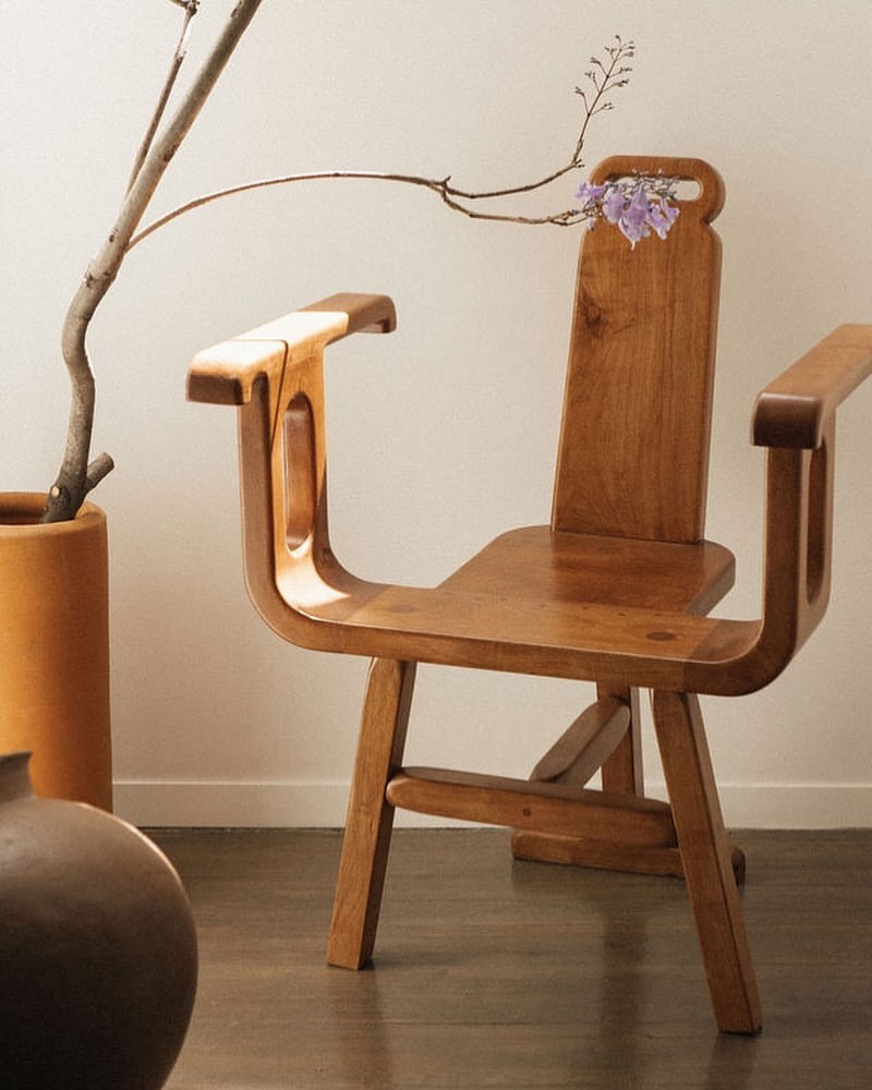 Wooden chair with purple flowers in a minimalist setting featuring a vase and neutral tones. The chair is the dominant element.