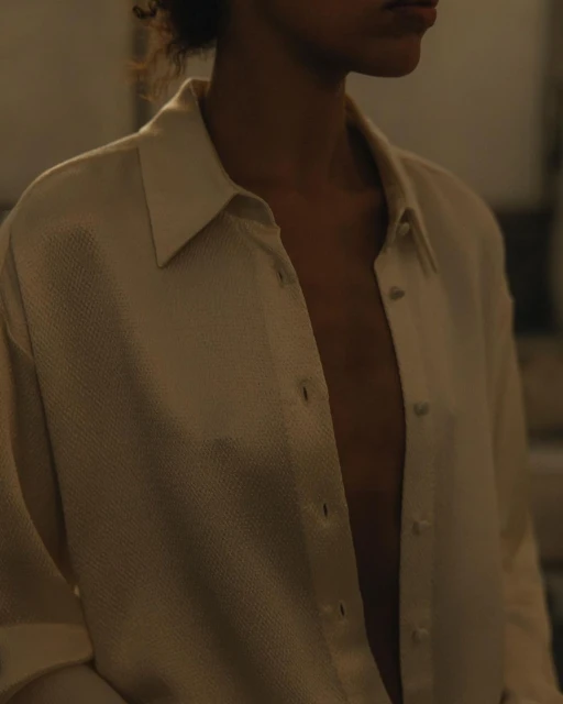 Close-up studio portrait of an adult woman with curly hair wearing an unbuttoned tan shirt, revealing her chest and collarbones.