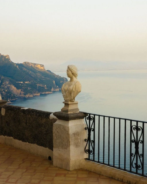 Scenic view of Amalfi Coast featuring a classical sculpture bust on a terrace overlooking the ocean and mountains at daytime, Italy.