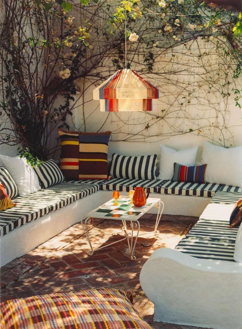 Outdoor patio featuring a corner built-in bench with striped cushions, throw pillows, a tiled coffee table, and a hanging lamp.