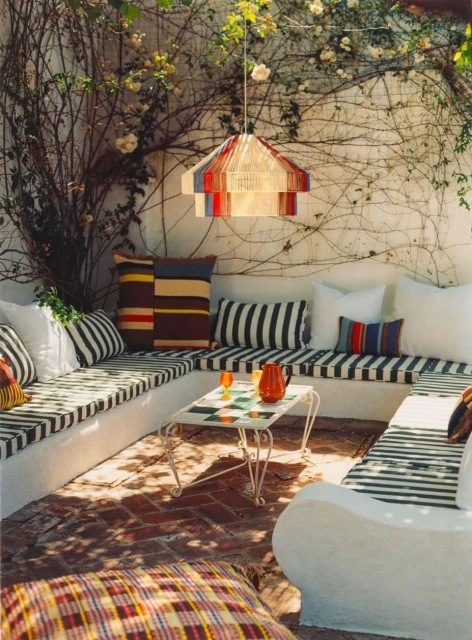 Outdoor patio featuring a corner built-in bench with striped cushions, throw pillows, a tiled coffee table, and a hanging lamp.
