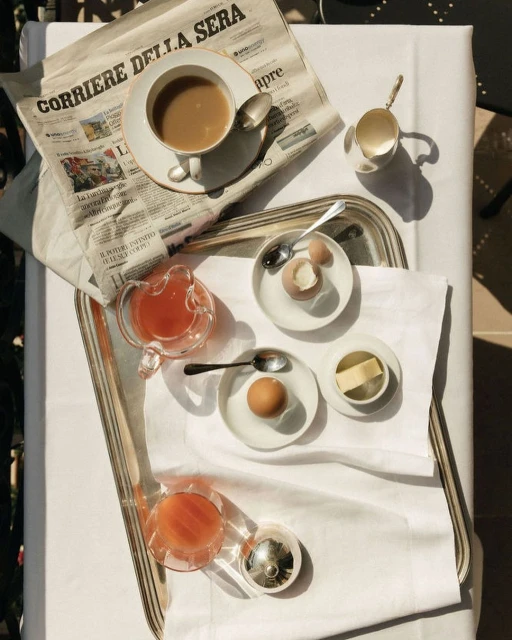 Breakfast table setting with coffee, eggs, juice, and newspaper. Tablecloth and natural lighting create a bright, inviting scene.