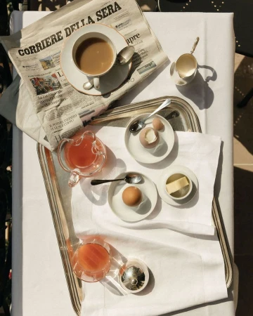 Breakfast table setting with coffee, eggs, juice, and newspaper. Tablecloth and natural lighting create a bright, inviting scene.
