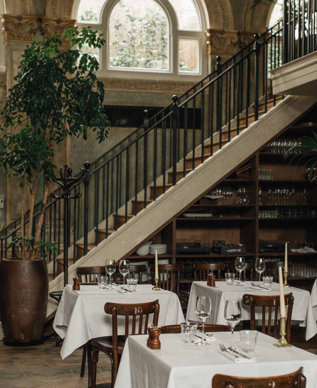 Indoor dining area features tables set with wine glasses, silverware, and white tablecloths, illuminated by soft light.