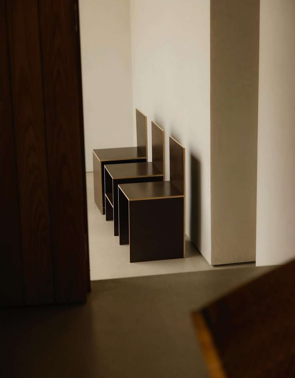 A row of modern, minimalist cube chairs line a white wall in an indoor space, casting soft shadows on the floor.