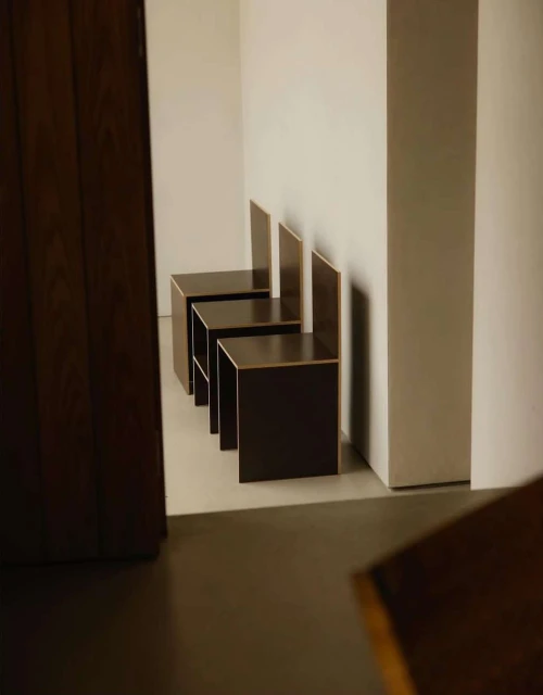 A row of modern, minimalist cube chairs line a white wall in an indoor space, casting soft shadows on the floor.