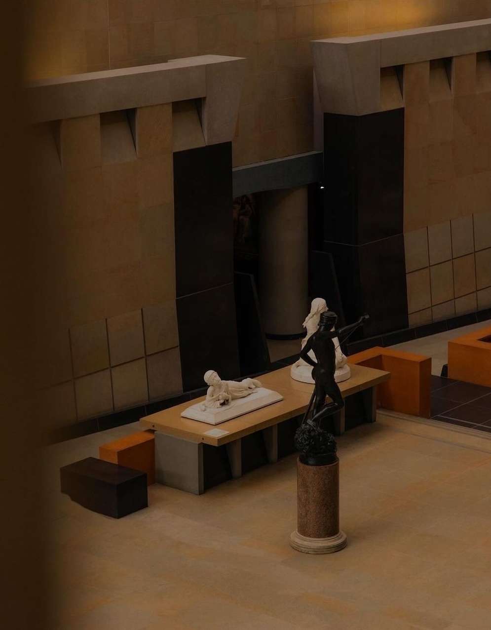 Indoor shot of three white, nude statue displays on platforms in a museum-like setting, with tan walls and dark accents.