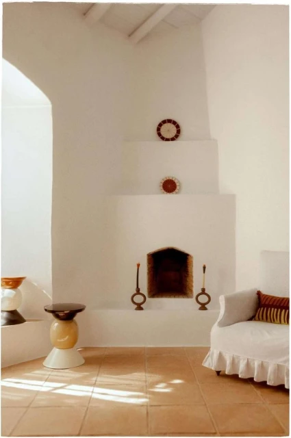 Minimalist interior design featuring a white fireplace, round sofa, ceramic table, and natural light creating a warm, inviting atmosphere.